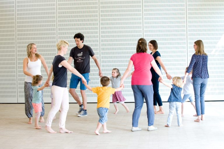Gruppentanz Eltern und Kinder fassen sich an den Händen und bewegen sich singend im Kreis.
