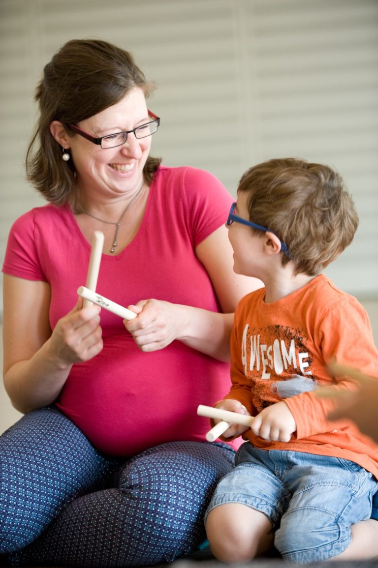 Gemeinsam musizieren und Begeisterung teilen. Mutter und Sohn spielen mit den Klanghölzern und gucken sich dabei begeistert und lachend an.